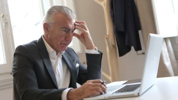 Foto de un hombre mayor angustiado sentado frente a su laptop