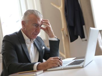 Foto de un hombre mayor angustiado sentado frente a su laptop
