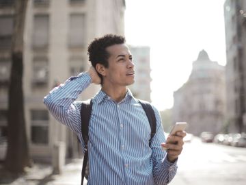 Foto de hombre pensativo usando su smartphone en la calle