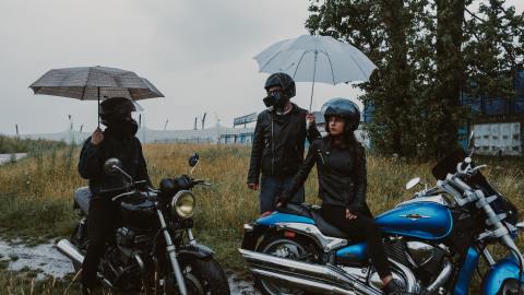 Foto de tres motociclistas con paraguas estacionados bajo la lluvia