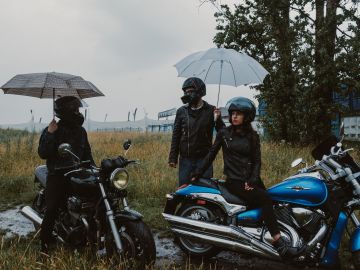 Foto de tres motociclistas con paraguas estacionados bajo la lluvia
