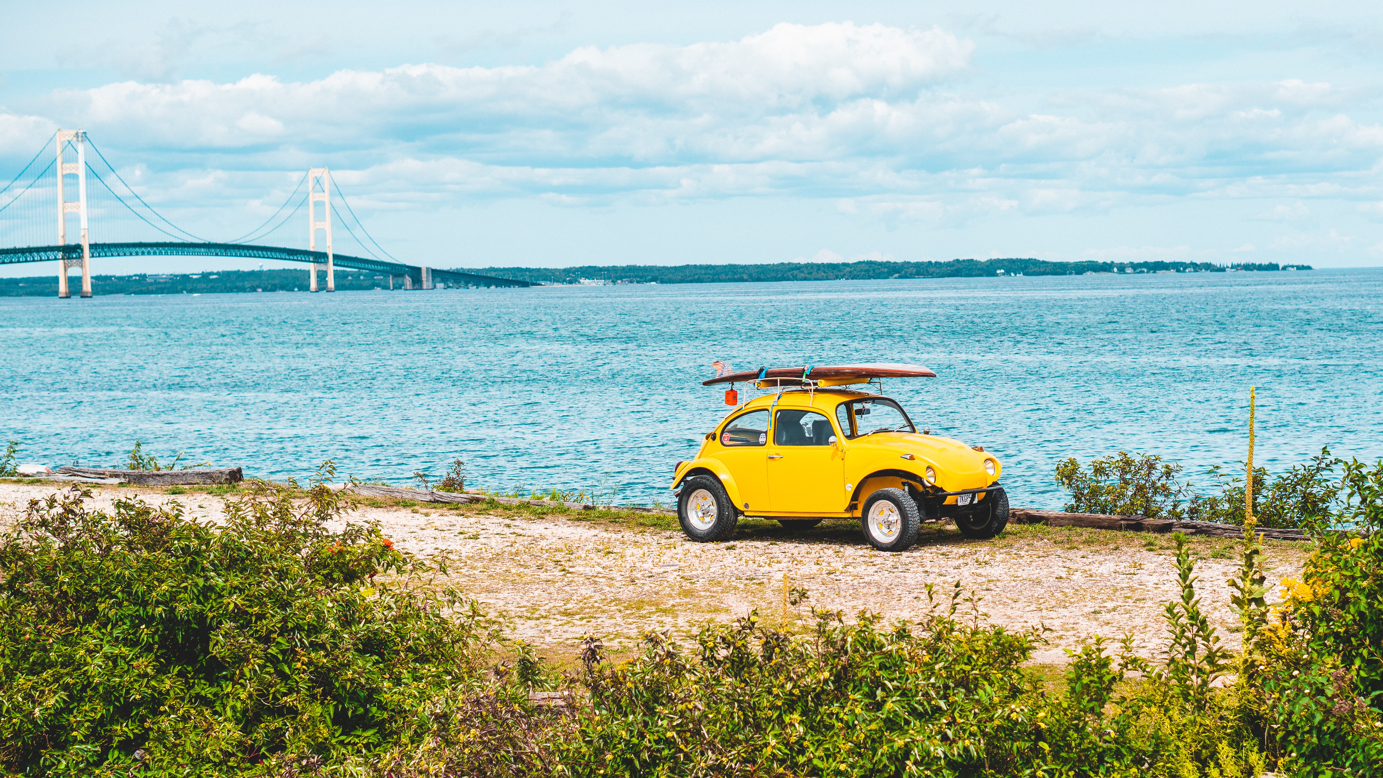 Foto de un Volkswagen escarabajo amarillo con una tabla de surf a la orilla del mar