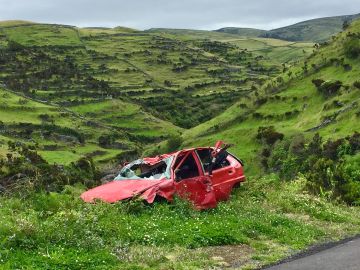 Foto de un auto destruido y abandonado a un lado de la carretera