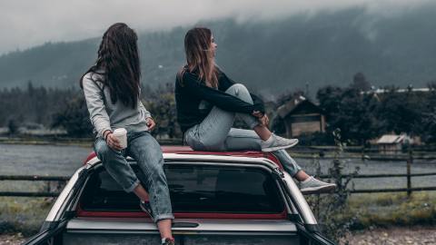 Foto de dos mujeres jóvenes sentadas sobre la cabina de una camioneta mientras contemplan el paisaje