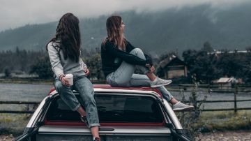 Foto de dos mujeres jóvenes sentadas sobre la cabina de una camioneta mientras contemplan el paisaje