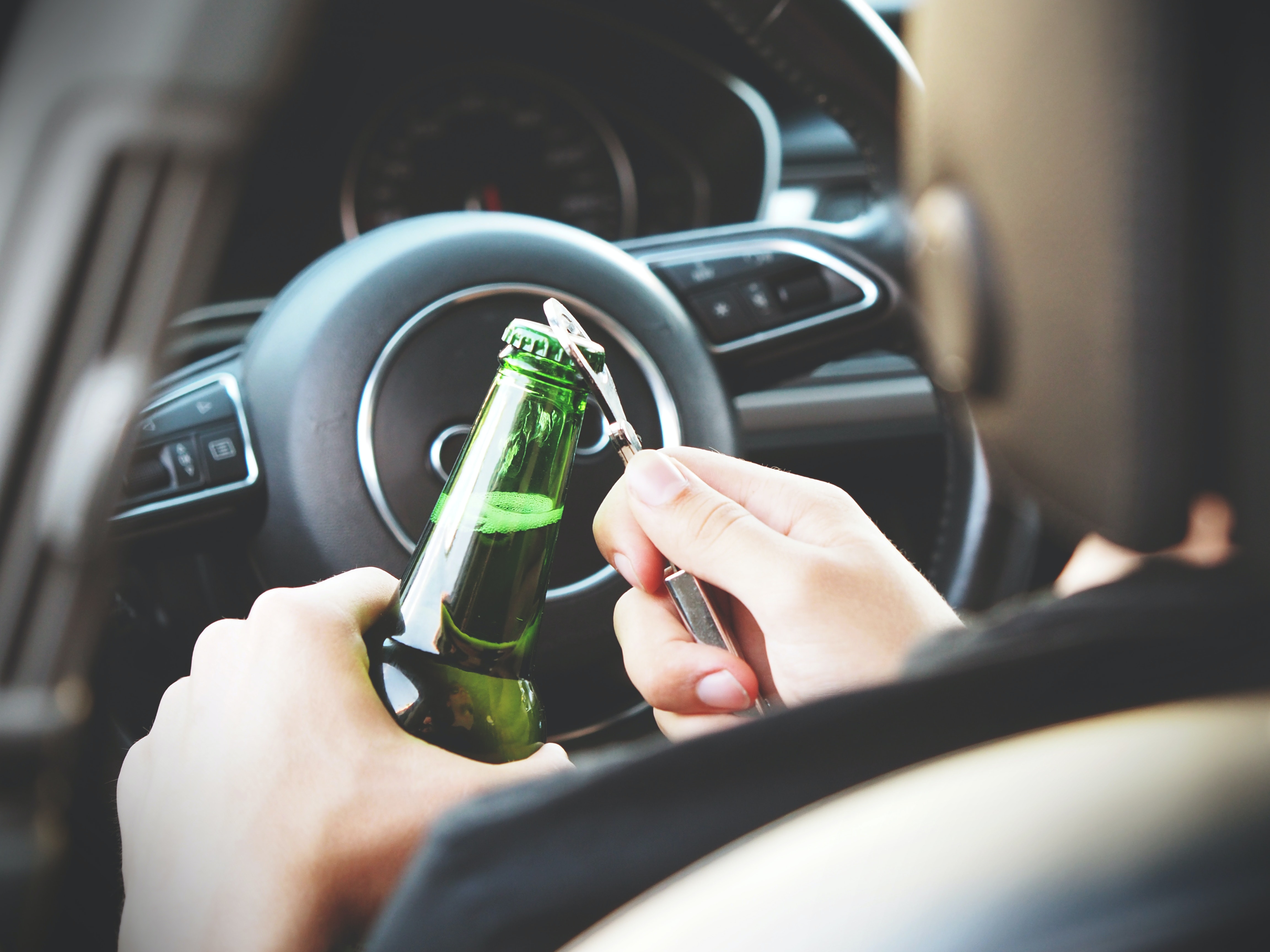 Foto de un hombre abriendo una botella de cerveza dentro de su auto