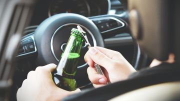 Foto de un hombre abriendo una botella de cerveza dentro de su auto