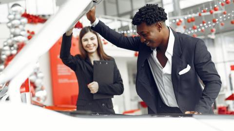 Foto de una vendedora mostrando el motor de un auto a un comprador