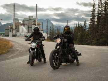 Foto de dos motociclistas con sus cascos estacionados en plena vía