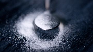 Foto de una cucharilla repleta de azúcar sobre una mesa con azúcar