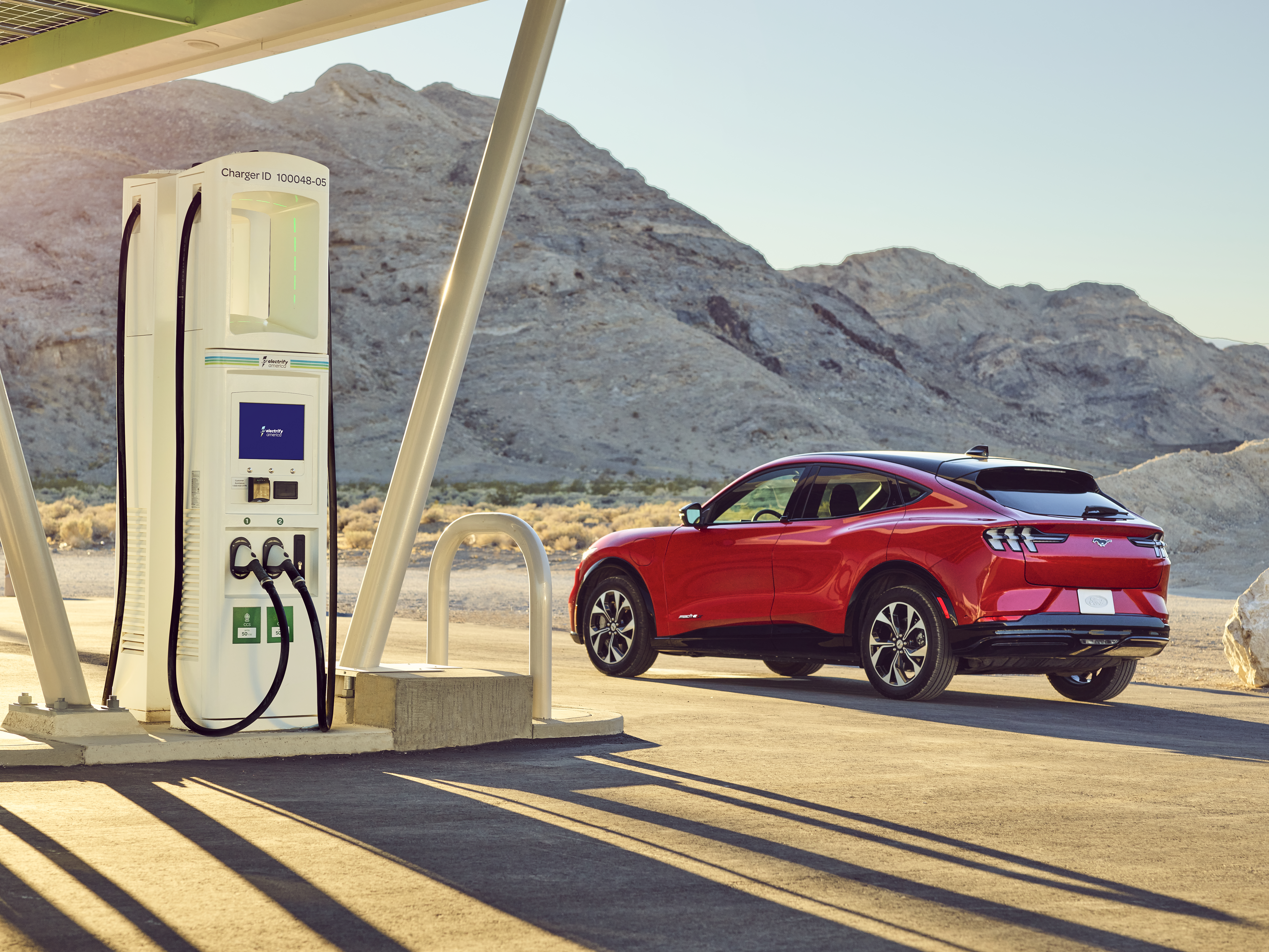 Foto de una estación de carga Electrify America con una SUV roja en segundo plano