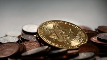 Foto de una pila de monedas entre las que se puede ver una con el logo distintivo de Bitcoin