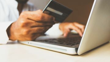 Foto de una persona sosteniendo una tarjeta de crédito frente a su laptop
