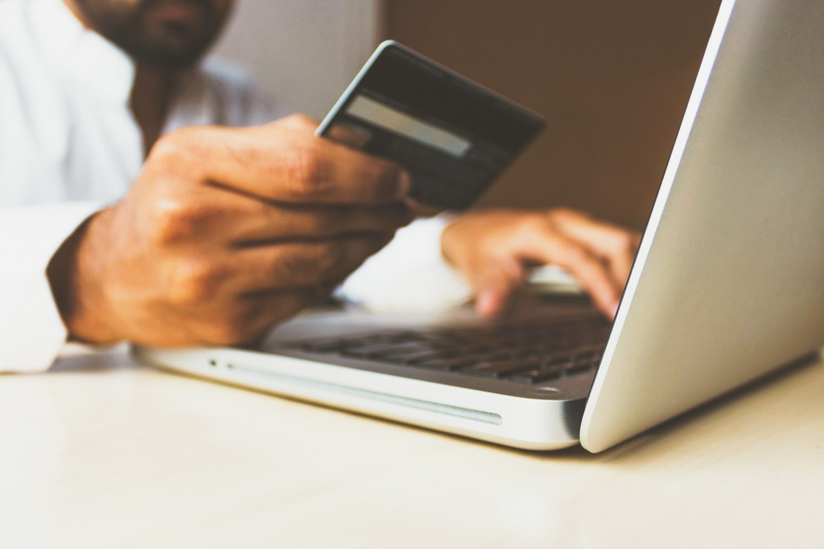 Foto de una persona sosteniendo una tarjeta de crédito frente a su laptop