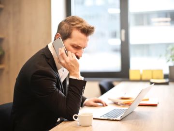 Foto de un ejecutivo en una oficina frente a una laptop mientras habla por teléfono.