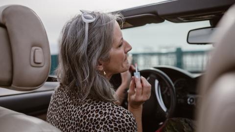 Foto de una mujer mayor frente al volante aplicándose labial.