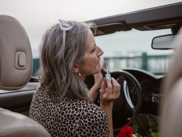 Foto de una mujer mayor frente al volante aplicándose labial.