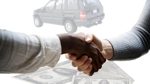 Foto de dos personas estrechándose las manos con un auto al fondo