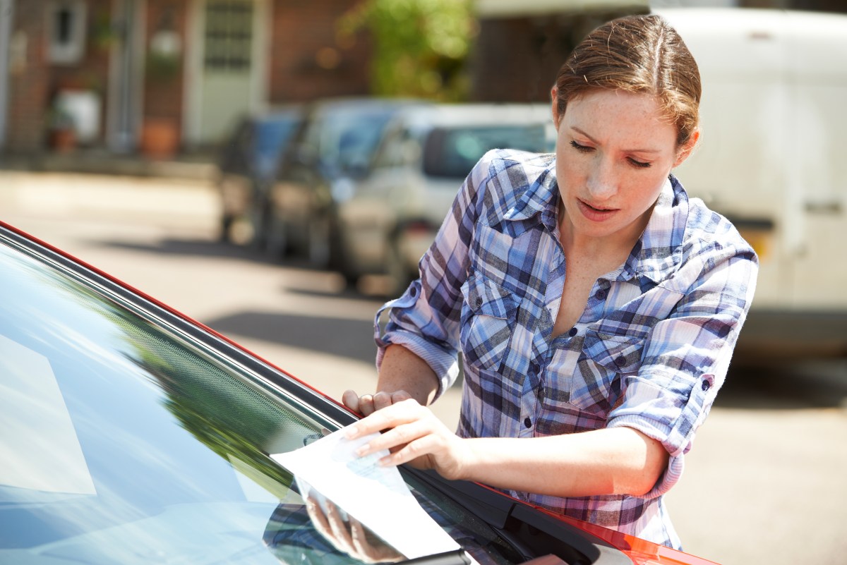 Foto de una mujer tomando una multa del parabrisas de su auto