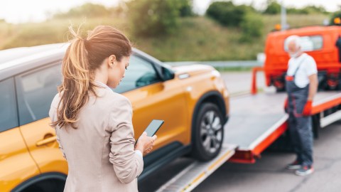 Foto de una mujer que usa el teléfono mientras su auto está siendo remolcado por la grúa