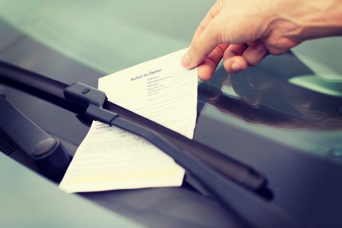 Foto de la mano de una persona recogiendo una multa de estacionamiento