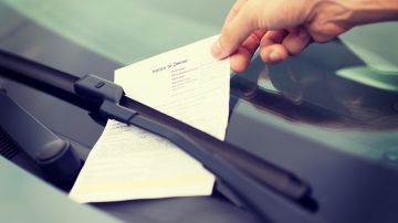 Foto de la mano de una persona recogiendo una multa de estacionamiento