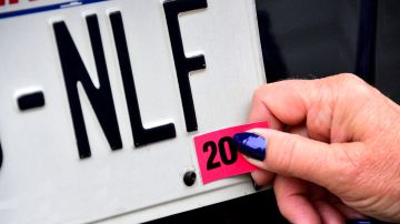 Foto de una persona colocando el sticker de registro en una placa de matrícula