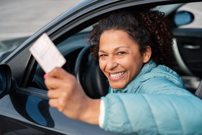 Foto de una mujer mostrando una tarjeta desde la ventana de un auto que conduce