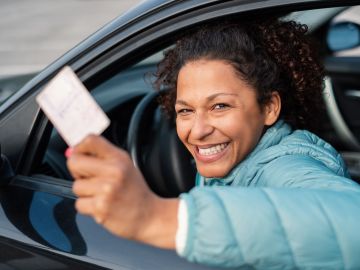 Foto de una mujer mostrando una tarjeta desde la ventana de un auto que conduce