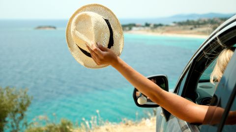 Foto de una mujer al volante con un sombrero en la mano