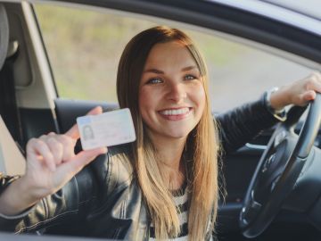 Foto de una mujer al volante con una licencia en su mano