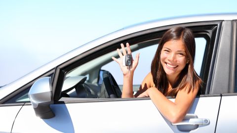 Foto de una mujer sonriente mostrando unas llaves desde su vehículo