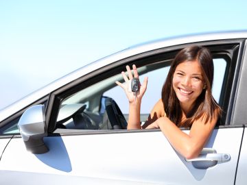 Foto de una mujer sonriente mostrando unas llaves desde su vehículo