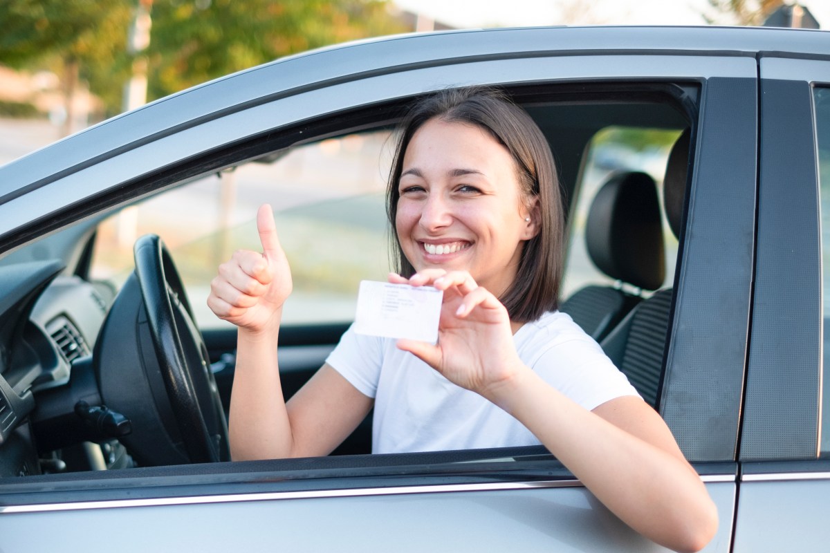 Foto de una mujer mostrando una licencia de conducir desde su auto
