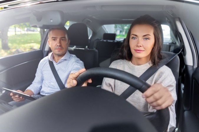 mujer latina conduciendo un auto con la ayuda de un experto que le enseña las maniobras de manejo