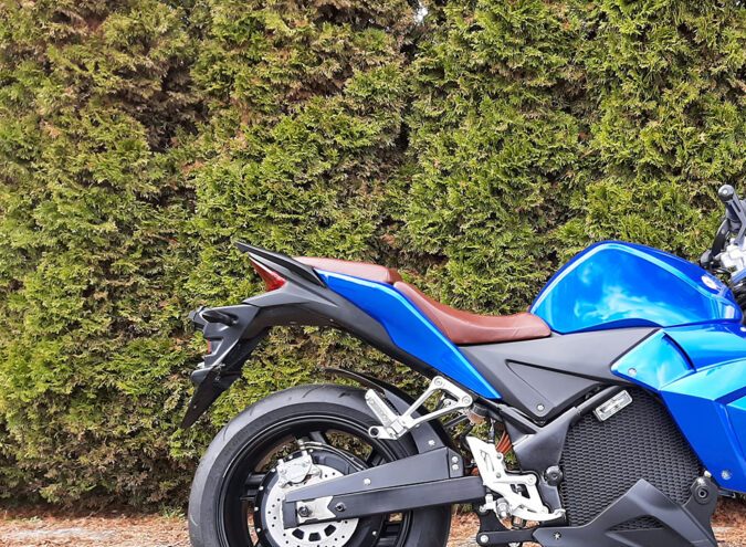 Evoke Urban Classic azul junto a arbustos, scooter eléctrico accesible con 156 millas por carga