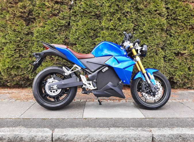 Evoke Urban Classic azul junto a arbustos, scooter eléctrico accesible con 156 millas por carga