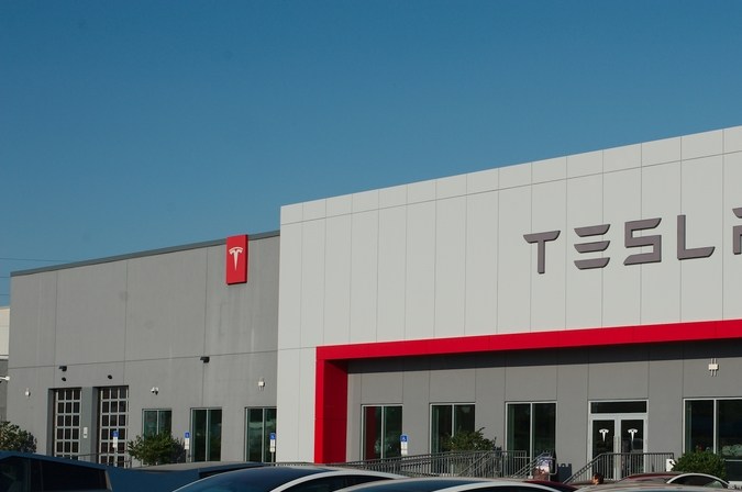 Fachada de una tienda Tesla con el logo de la marca en la parte superior y varios Model 3 y Model X blancos estacionados frente al edificio.