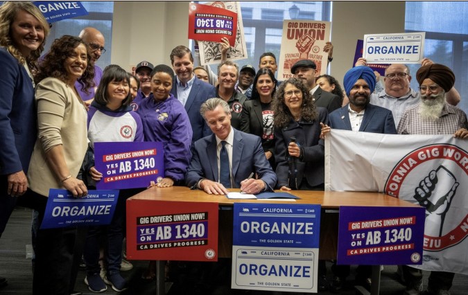 El gobernador de California, Gavin Newsom, firma la ley AB 1340 rodeado de conductores de Uber y Lyft que celebran el nuevo derecho a sindicalizarse.