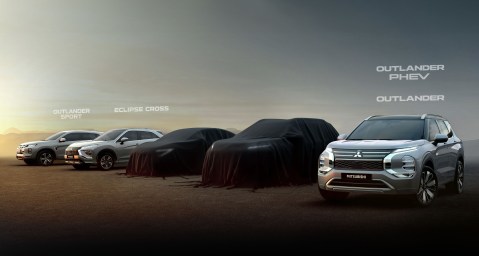 Exhibición de varios modelos de Mitsubishi, incluyendo un Outlander y otros SUVs cubiertos, en un escenario al atardecer