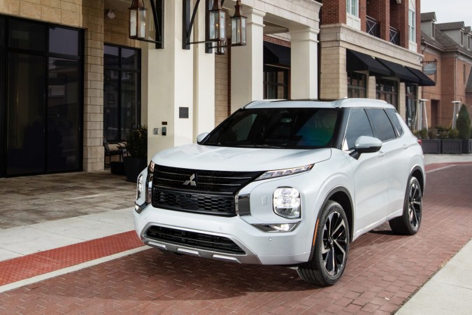 SUV blanco de Mitsubishi, modelo Outlander estacionado frente a un edificio elegante, mostrando su parrilla frontal distintiva y diseño urbano.
