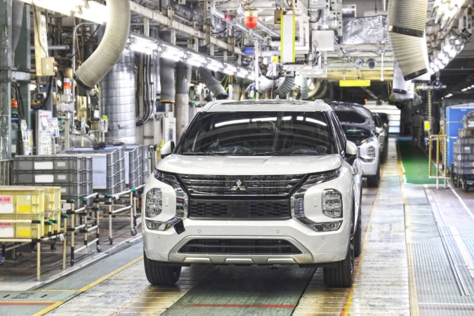 Mitsubishi Outlander, SUV blanco en una línea de ensamblaje de fábrica, con maquinaria y equipo industrial al fondo.