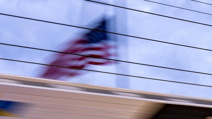 Autos Porsche 963 compitiendo en un circuito nocturno con bandera estadounidense al fondo.