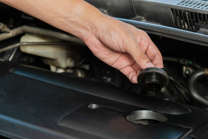 Mano retirando tapón de aceite de motor, guía para diagnóstico y solución de problemas en automóviles.