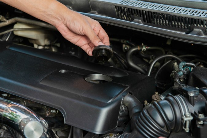 Mano retirando tapón de aceite de motor, guía para diagnóstico y solución de problemas en automóviles.