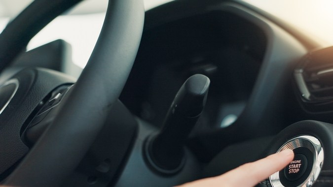 Mano presionando el botón de encendido Start-Stop en el interior de un auto moderno, con el volante y la consola visibles.