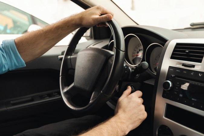 Mano girando la llave de encendido en un auto clásico, con el volante y el tablero de instrumentos a la vista.