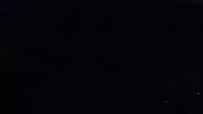 El automóvil autónomo Waymo cruza una intersección por la noche, iluminado por farolas, con peatones caminando y semáforos en el fondo.