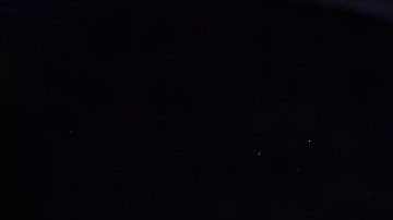 El automóvil autónomo Waymo cruza una intersección por la noche, iluminado por farolas, con peatones caminando y semáforos en el fondo.