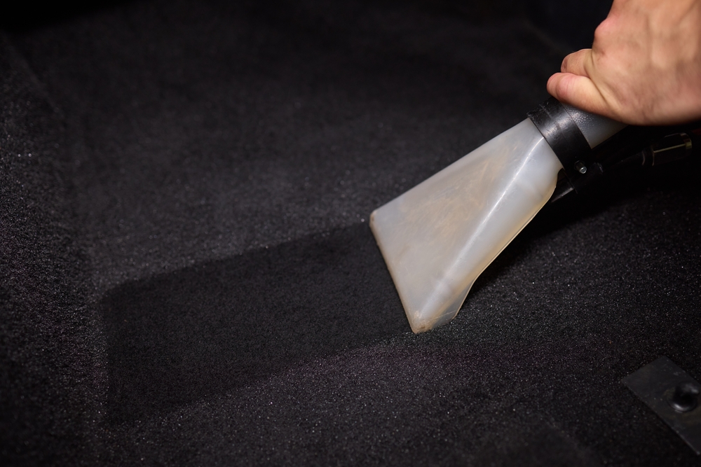 Una mano profesional que utiliza una herramienta de extracción de vacío para limpiar en profundidad una alfombra de coche, mejorando su limpieza.